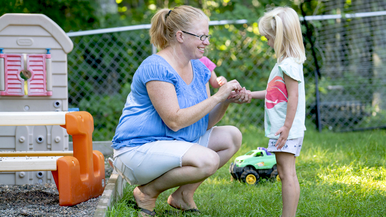 Licensed child care provider interacting with girl outside in a yard