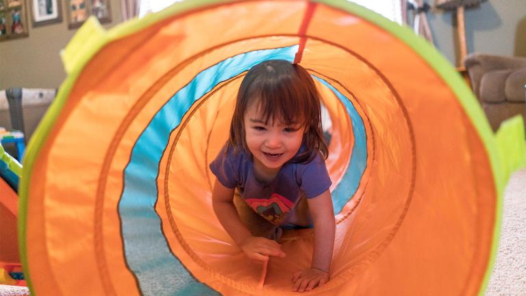 Toddler girl smiling and crawling in colorful tunnel at family child care